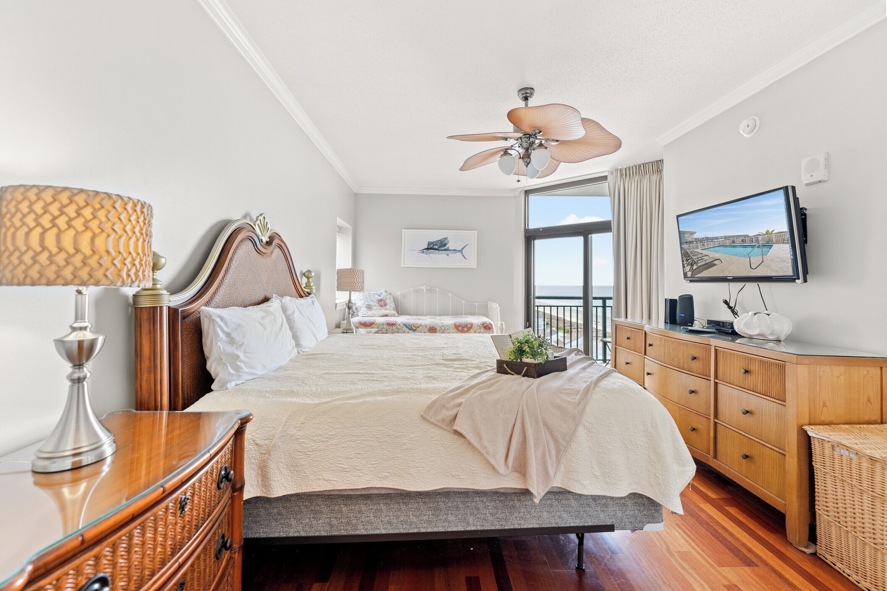 Une chambre à coucher comprenant un lit, des tables de chevet, une commode, un téléviseur et un ventilateur de plafond.