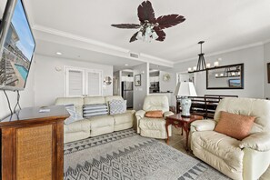 Un salon doté d’un ventilateur de plafond, d’un téléviseur et d’un coin repas agrémenté d’un lustre.