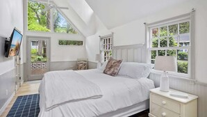 A bedroom with a large bed, a nightstand, a TV, and a window with a view of greenery. - 1min to Private Beach, High-end Design & Hot tub (New Buffalo)
