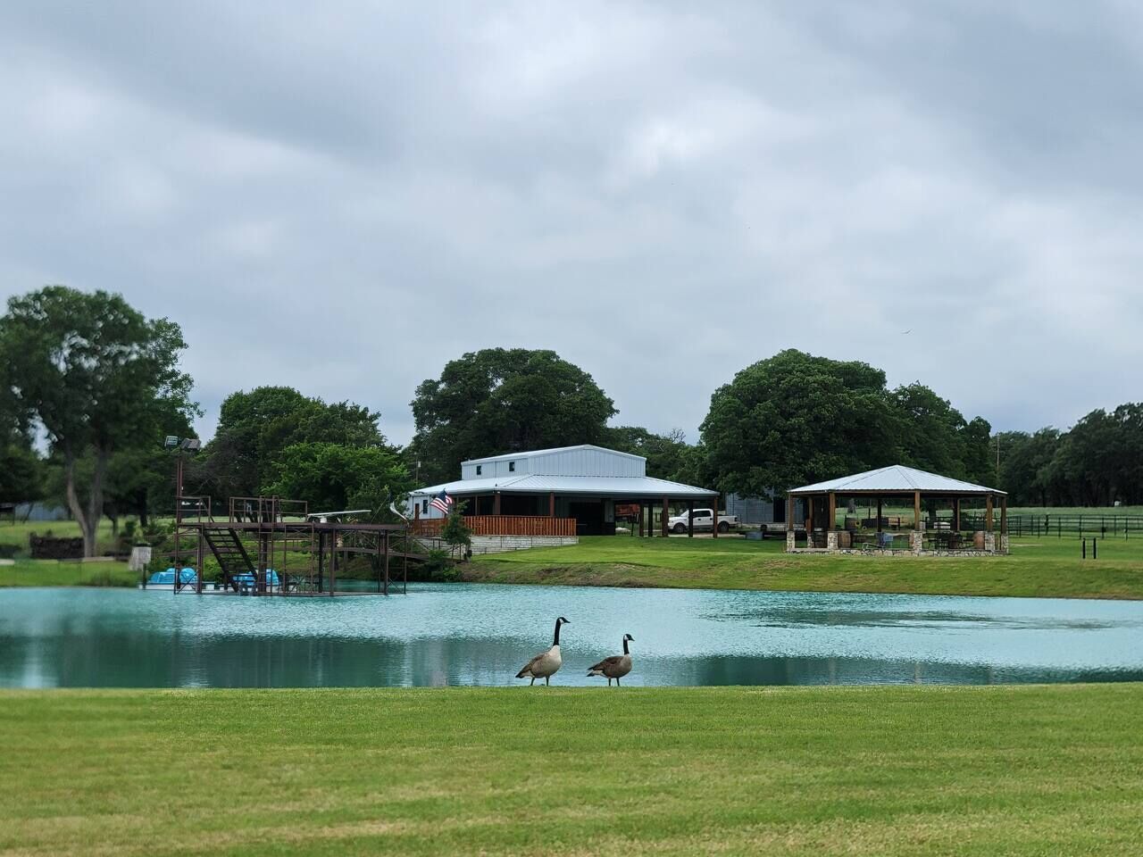 A park with a pond, a gazebo, and a building with a flag.