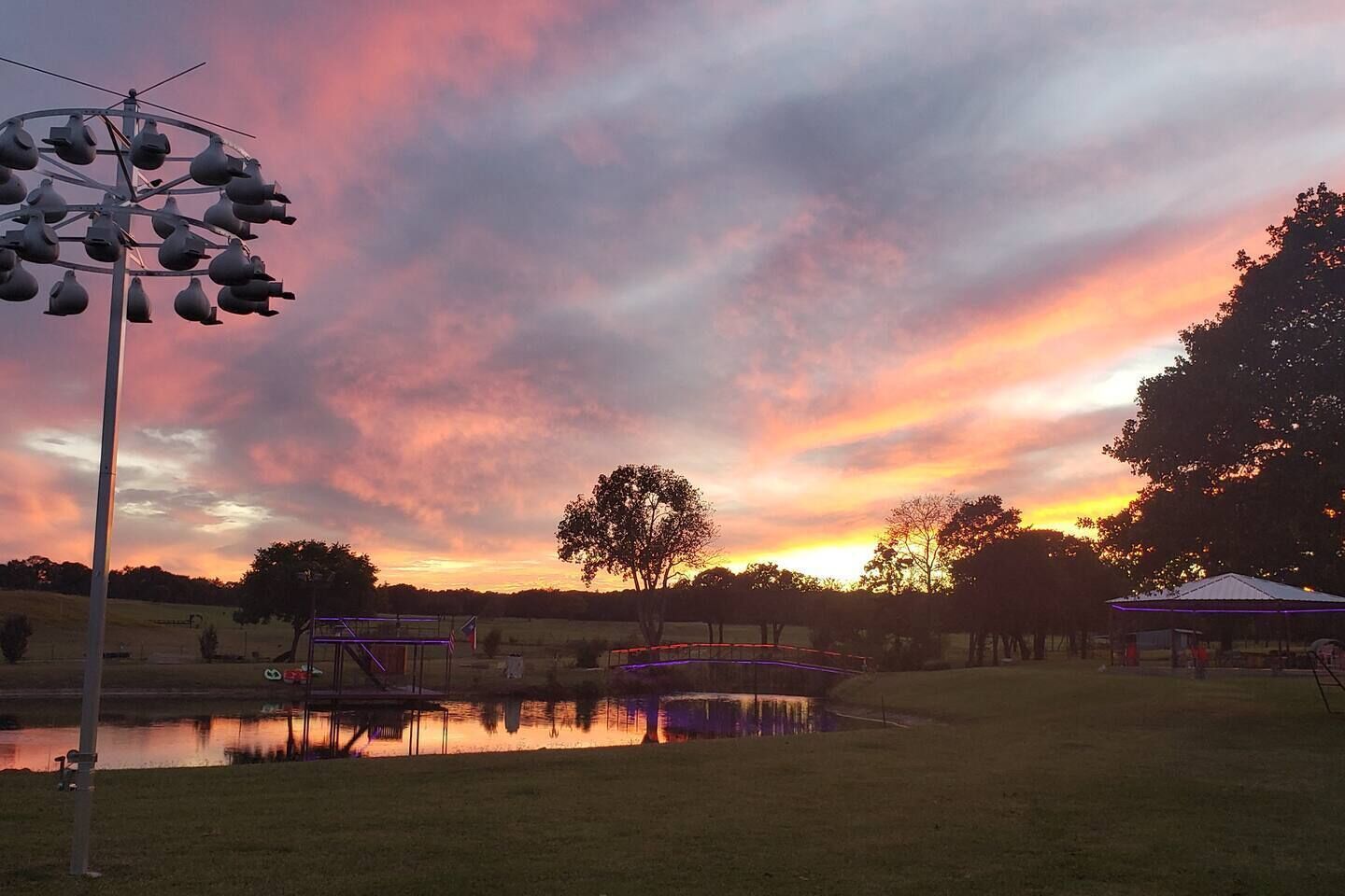 A park with a playground, a pond, and a sunset sky.
