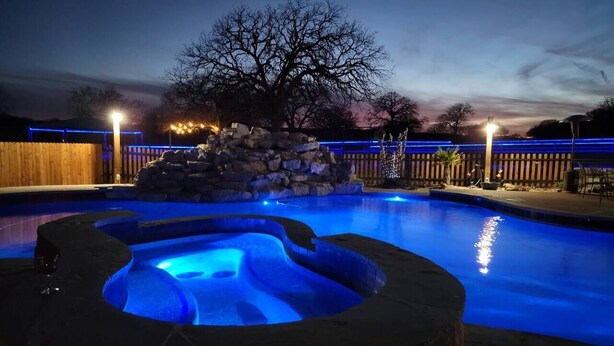 A swimming pool with a hot tub and a stone feature, surrounded by a wooden fence and trees. - Harley-Davidson Cabana at Tipsy Toad Retreat (Boyd)