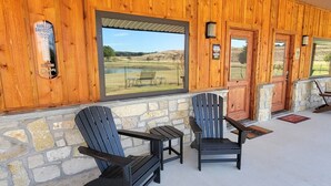 A covered porch with Adirondack chairs, a stone wall, and a view of a rural landscape. - Harley-Davidson Cabana at Tipsy Toad Retreat (Boyd)
