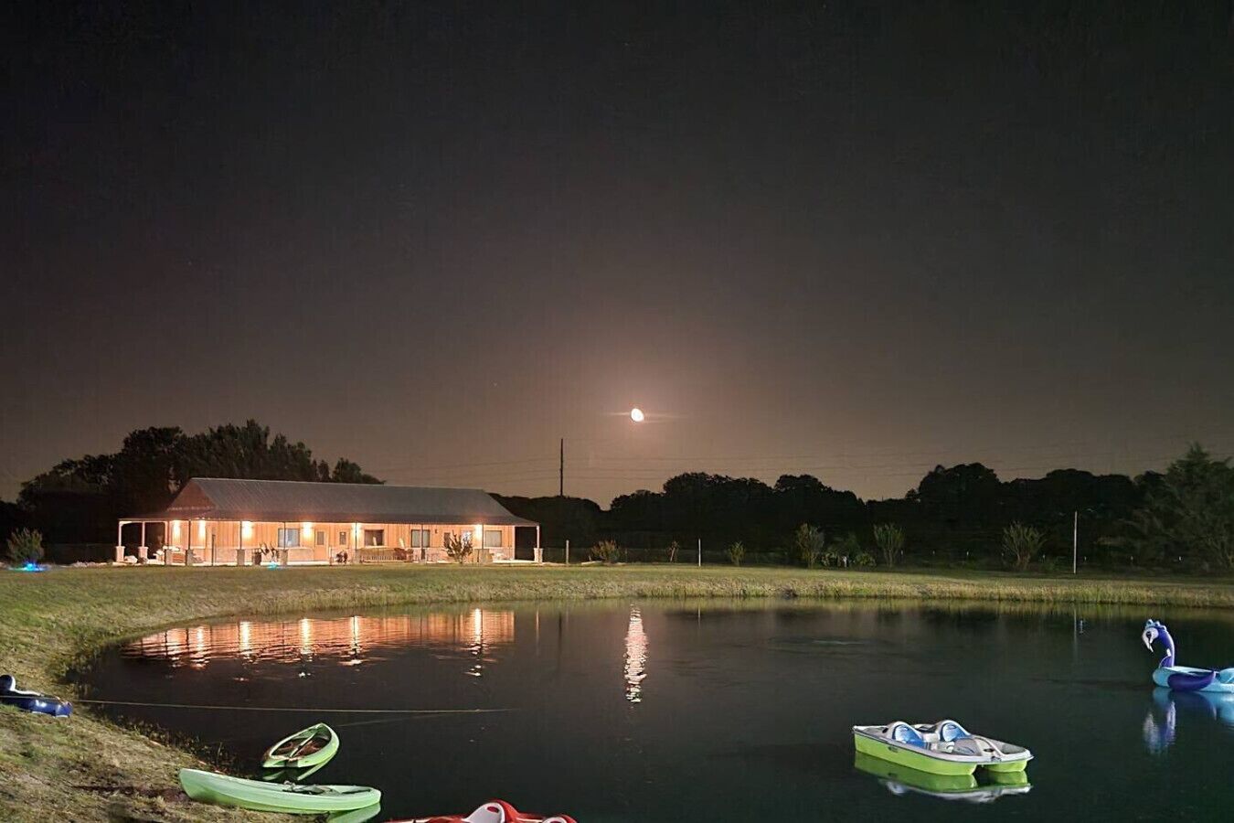 Un edificio con un estanque reflectante, barcas y una luna en el cielo.