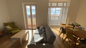 Ein Wohnzimmer mit einer Couch, einem Couchtisch, einem Esstisch mit Stühlen und einem Balkon mit Blick.