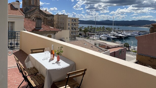 Ein Balkon mit gedecktem Tisch für zwei Personen, mit Blick auf eine Marina mit Booten und einem historischen Gebäude mit Kuppel.