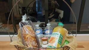 Ein Korb mit Brot, Wasserflaschen, einer Saftflasche und einem kleinen Behälter auf einer Holztischplatte.