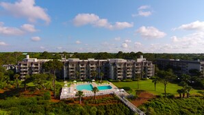 A hotel with multiple floors, a central swimming pool, and surrounding greenery. - Ocean One 121 - Oceanfront 1st Floor Condo (Hilton Head Island)