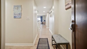 A hallway with a bench, a welcome sign, and a door. - Ocean One 121 - Oceanfront 1st Floor Condo (Hilton Head Island)