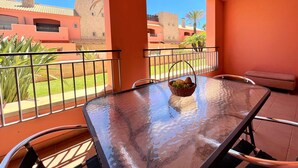 Un balcón con una mesa de vidrio, sillas y una cesta de frutas.