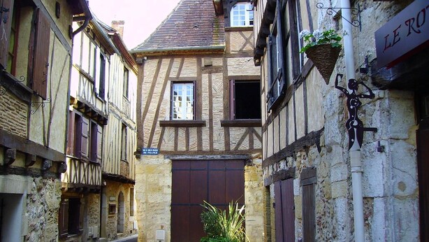Eine enge Straße mit traditionellen Fachwerkhäusern, einer großen Holztür und einem Schild mit der Aufschrift 'LE ROY'.