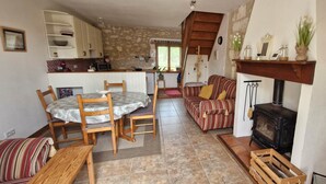 Ein gemütliches Wohnzimmer mit Kamin, ein Essbereich mit Tisch und Stühlen, eine Küche mit weißen Schränken und ein gestreiftes Sofa.