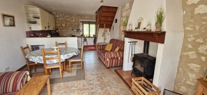 A cozy living room with a fireplace, a dining area with a table and chairs, a kitchen with white cabinets, and a striped sofa. - Gîte Le Charpentier, charm and independence in the heart of a large park (Eyraud-Crempse-Maurens)