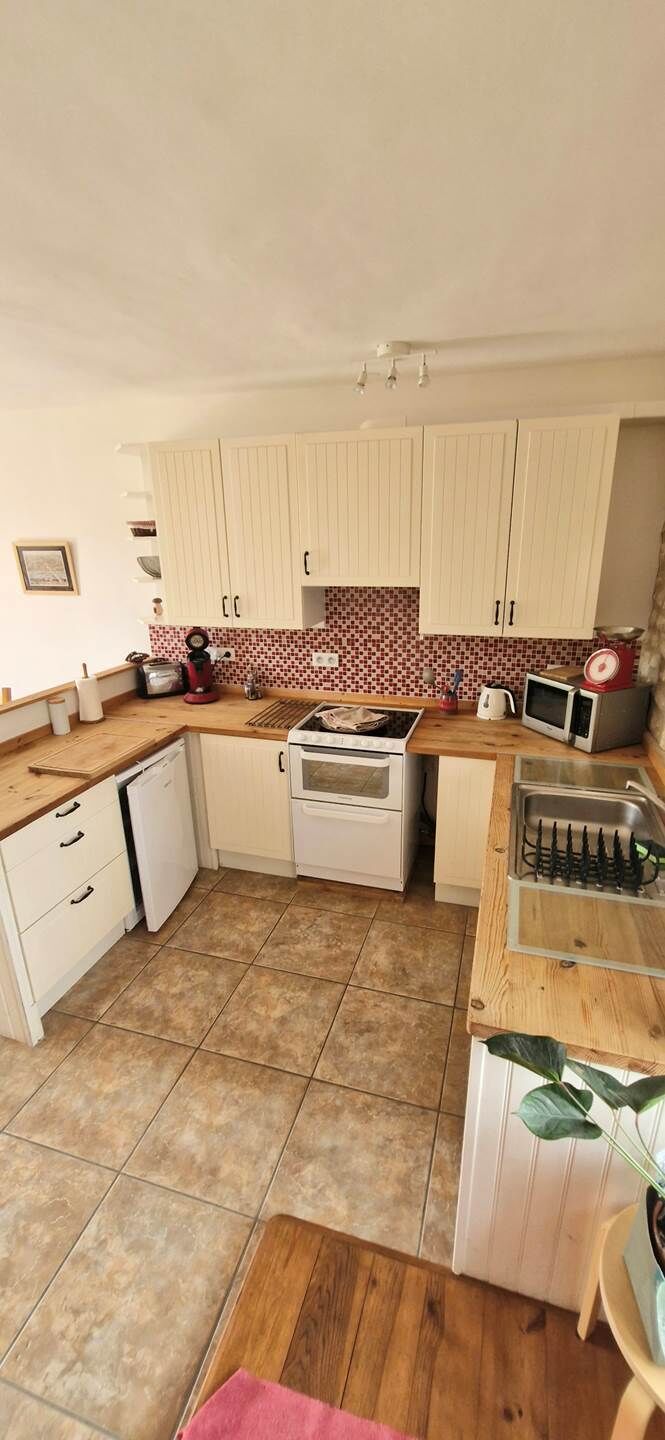 Una cucina compatta con mobili bianchi, piastrelle a parete, un forno a microonde e un lavandino.