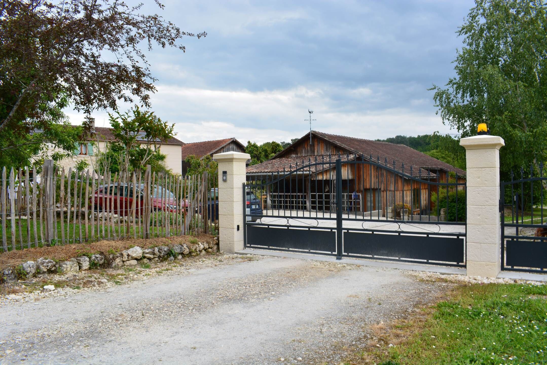 A gated entrance to a property with a gravel driveway leading to a house with a tiled roof.