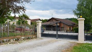 A gated entrance to a property with a gravel driveway leading to a house with a tiled roof.