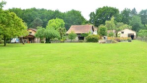 Ein grünes Feld mit einer Holzhütte und einem Steinhaus im Hintergrund.