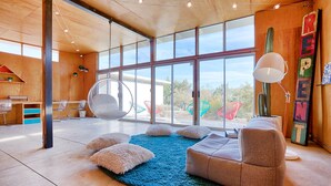 A spacious room with a large window, a blue rug, a hanging chair, and a cactus. - Creative Desert Retreat in the heart of Joshua Tree (Joshua Tree)