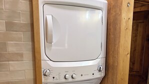 Un appareil compact combinant lave-linge et sèche-linge, doté d’un panneau de commande, installé devant un mur en bois et sur un sol carrelé.