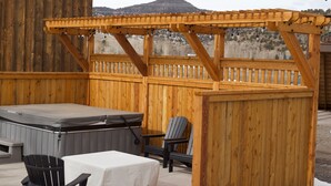 Une terrasse en bois avec un jacuzzi, un espace salon couvert et une vue sur les montagnes.