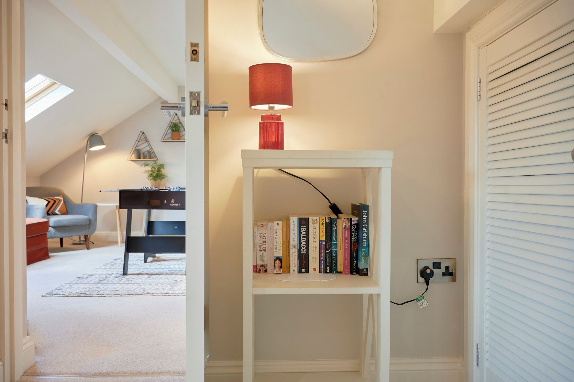 Ett rum med en vit bokhylla, en röd lampa och en taklampa. Det finns en dörr med ett fönster på vänster sida och en vit vägg med ett eluttag på höger sida.