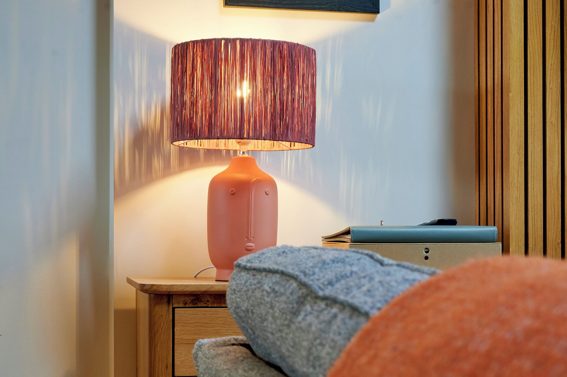 Une table de chevet avec une lampe, un petit tiroir et un portefeuille posé dessus.