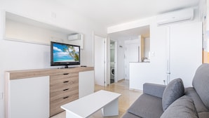 Un salon moderne avec un téléviseur à écran plat, un canapé gris, une table basse blanche et un meuble en bois.