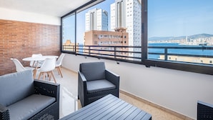 Un balcon agrémenté de meubles en osier, d’une table et offrant une vue sur le paysage urbain et la mer.