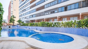 Une piscine à bord incurvé, entourée d’une terrasse carrelée et d’un petit muret en briques.