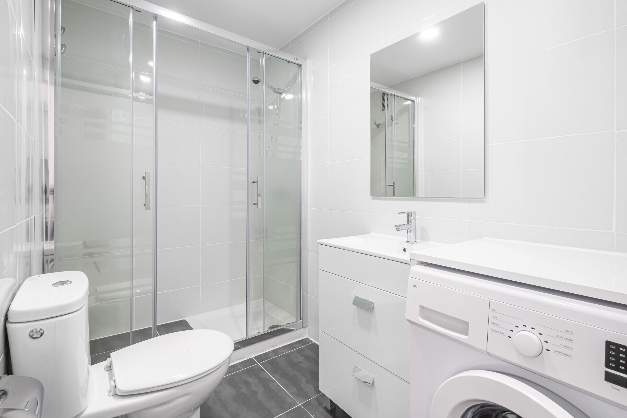 A modern bathroom with a glass-enclosed shower, a white toilet, and a built-in washing machine.