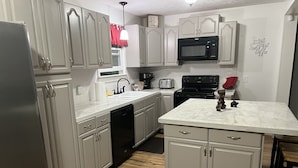 A kitchen with light grey cabinets, a black microwave, a stove, a sink, and a wooden floor.