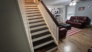 A staircase leading to a landing, a living room with a leather sofa, a coffee table, and a checkered rug.