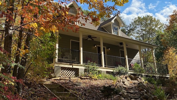 A house with a covered porch, stone steps, and a garden with autumn foliage.
