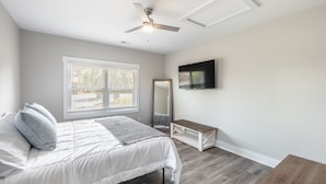 A bedroom with a bed, a ceiling fan, a window with blinds, a mirror, and a TV on the wall. - Spacious w/ all King Beds, 15 min from Beach + Downtown, Pup Friendly! (Wilmington)