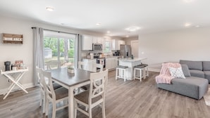 A modern kitchen with white cabinets, a central island, and a dining area with a table and chairs. - Spacious w/ all King Beds, 15 min from Beach + Downtown, Pup Friendly! (Wilmington)