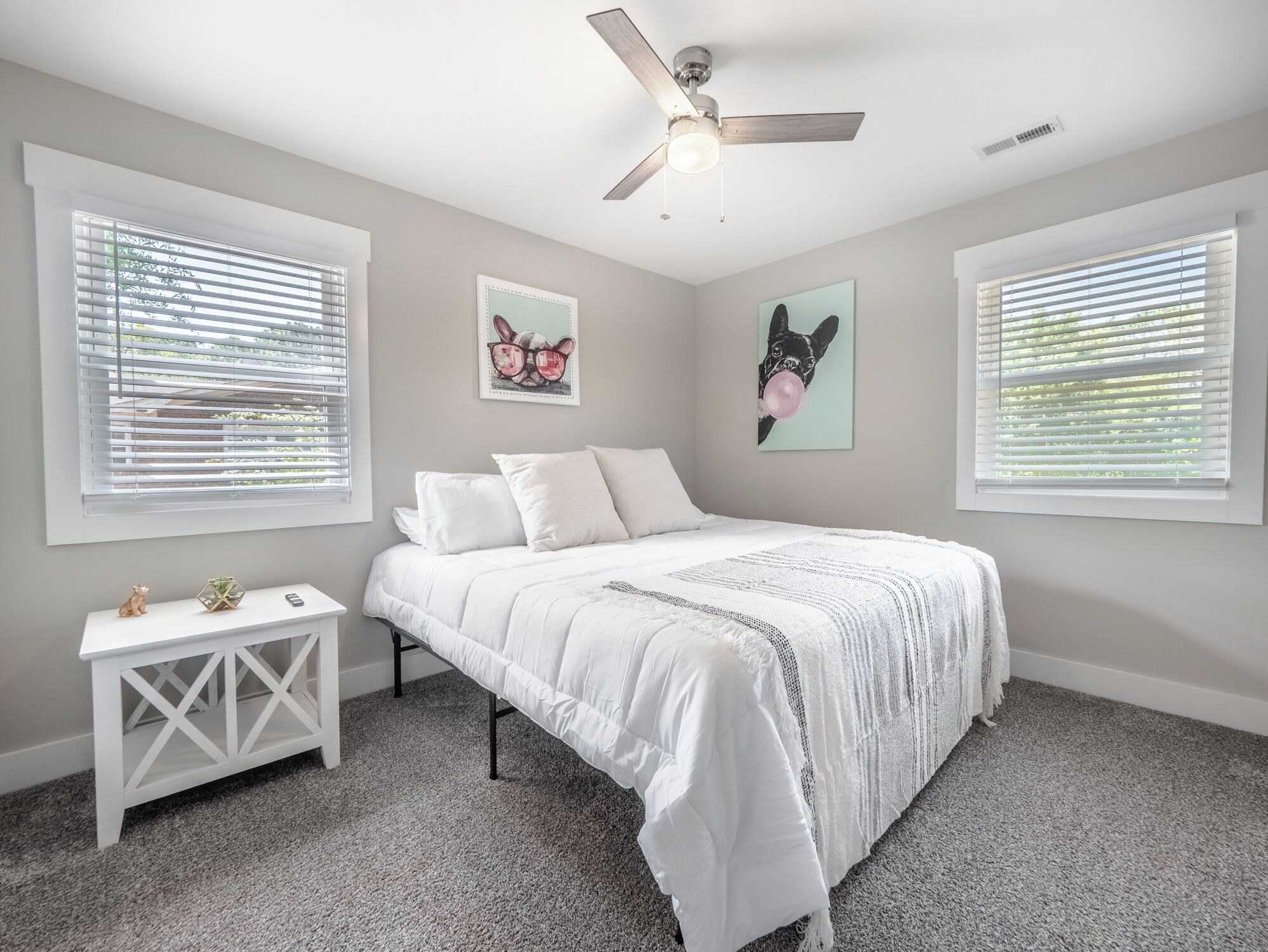 A bedroom with a bed, a nightstand, a ceiling fan, and two windows with blinds.