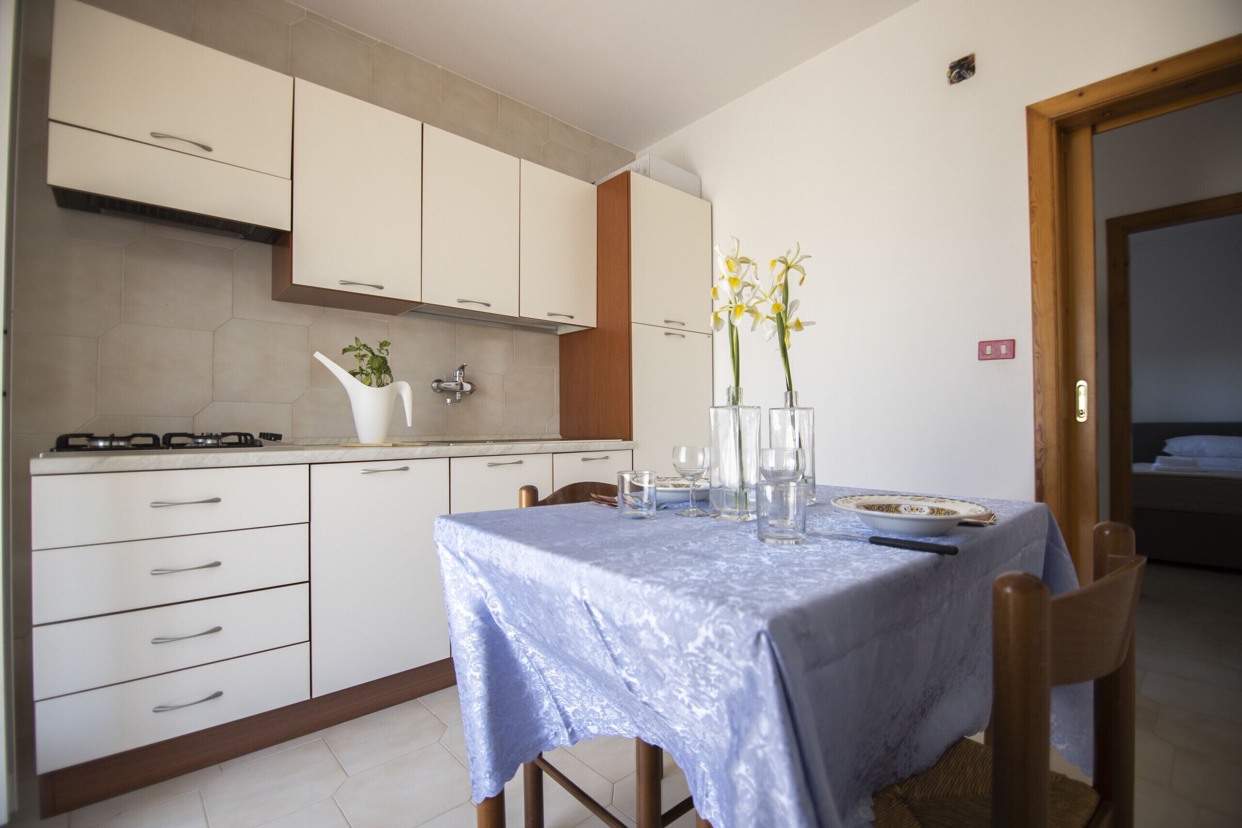 Une cuisine moderne avec des meubles blancs, une cuisinière à gaz et une table à manger dressée avec des assiettes, des verres et un vase de fleurs.