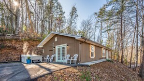 Une cabane dotée d’un porche à l’avant, d’un bain à remous et d’un espace patio avec des chaises.