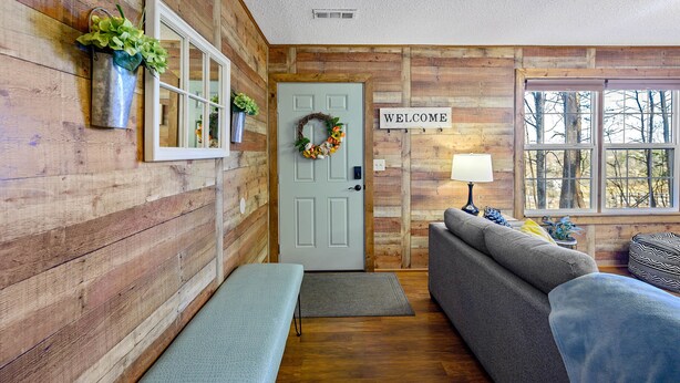 L’intérieur d’un chalet accueillant, avec un mur en bois, une pancarte de bienvenue, un banc, un canapé et une fenêtre donnant sur les arbres.