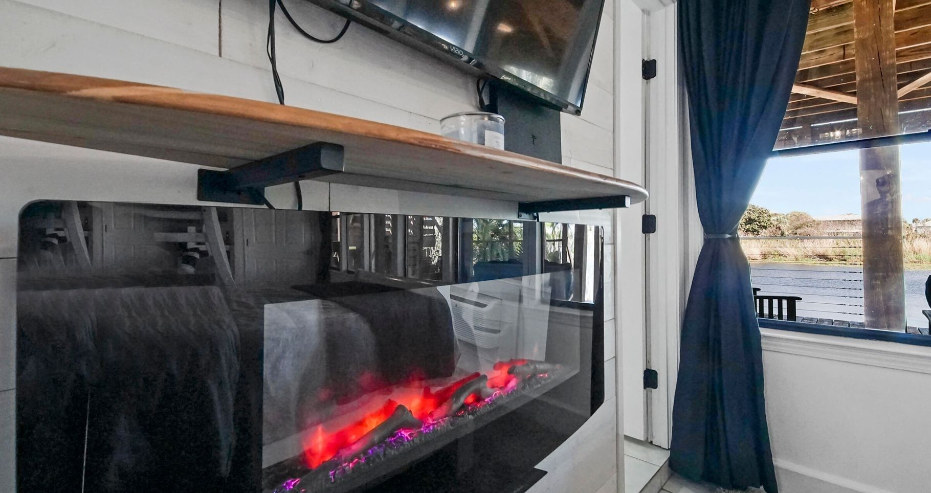 A modern kitchen with a built-in fireplace, a wooden shelf above the stove, and a window with a view of the outdoors.
