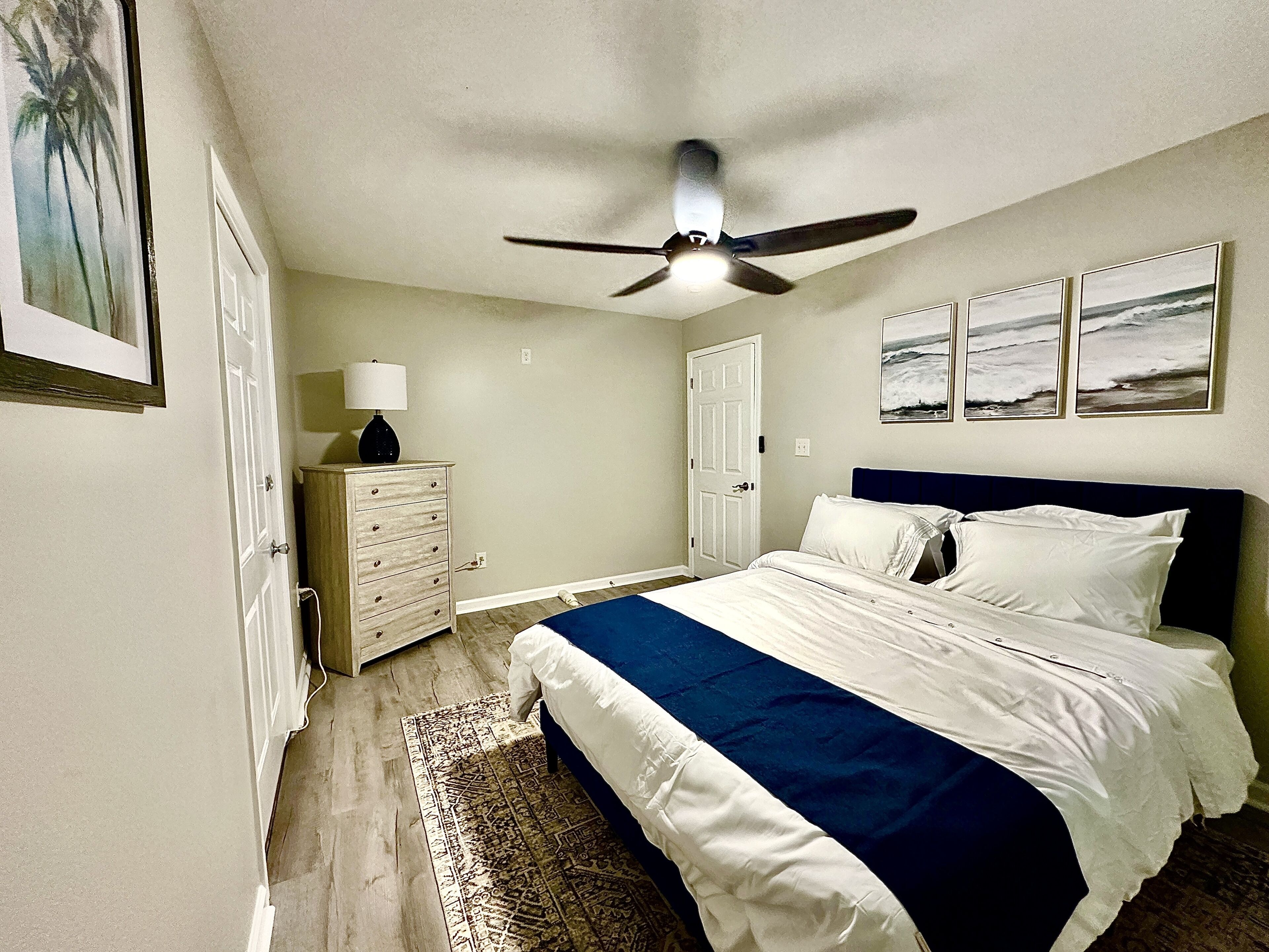A bedroom with a bed, a dresser, a ceiling fan, and framed pictures on the wall.