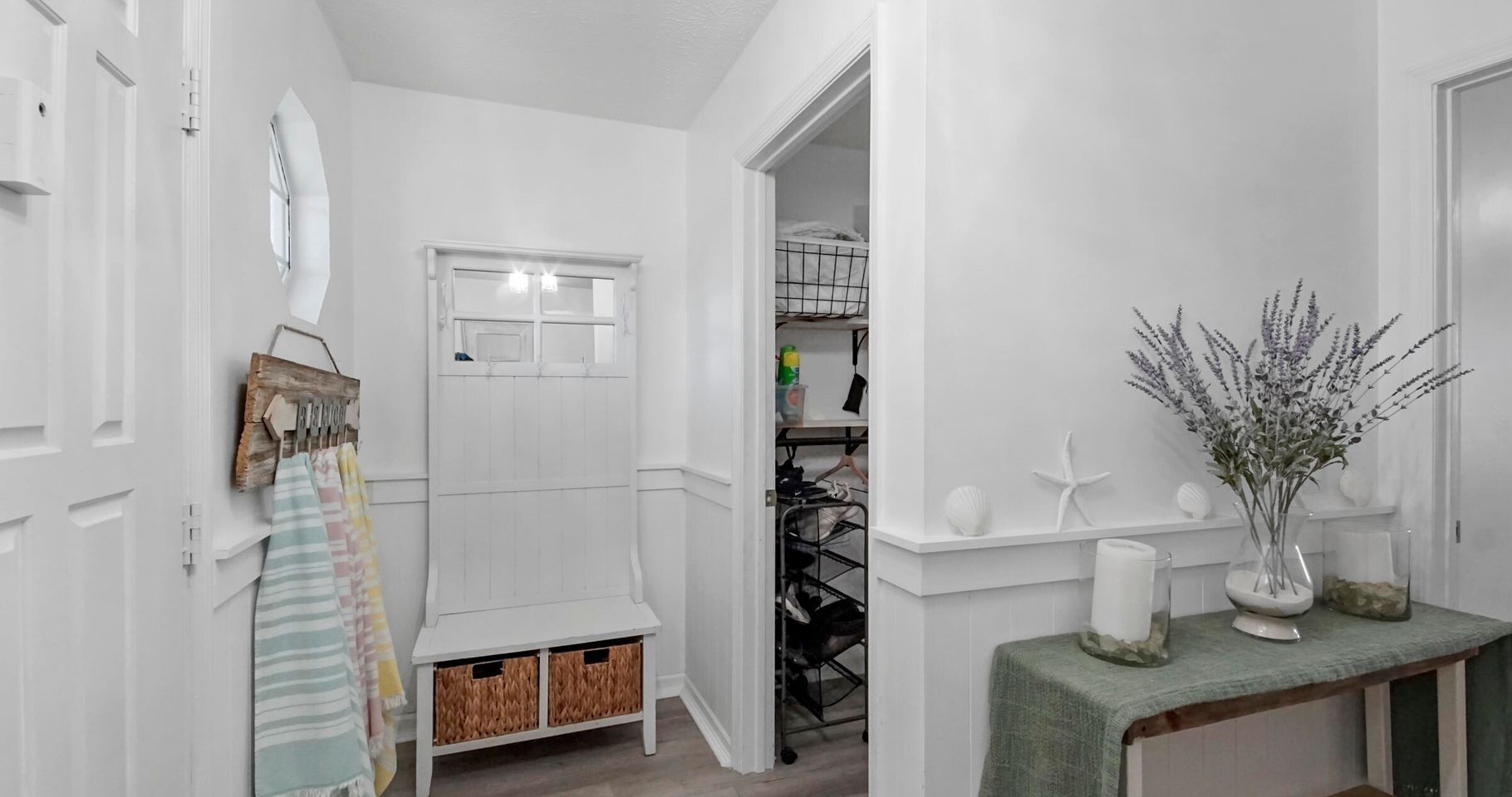 A hallway with a white door, a small bench, a basket, and a table with a vase.