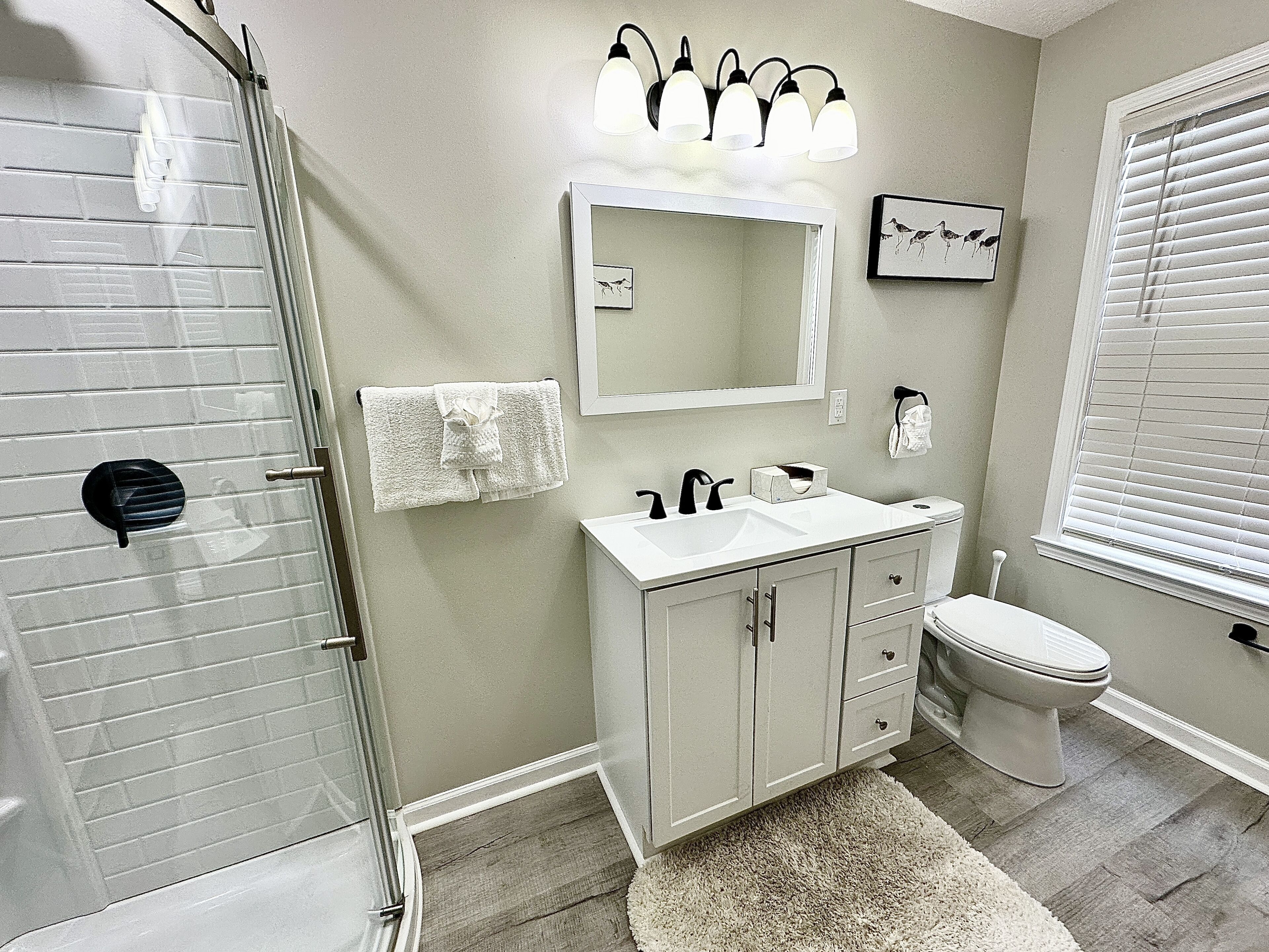 A bathroom with a glass shower enclosure, a white sink, a mirror, and a toilet.