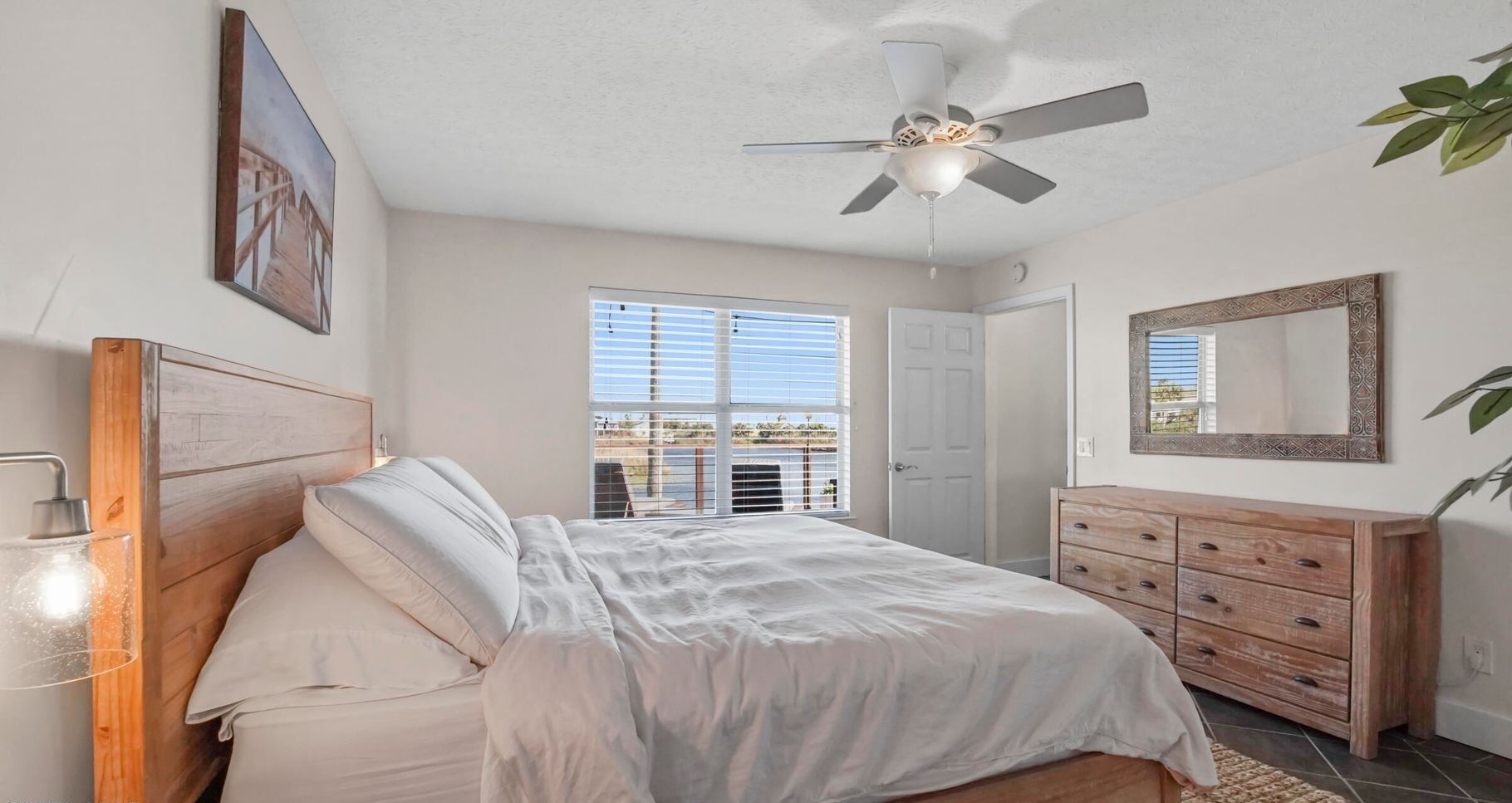 A bedroom with a bed, a ceiling fan, a dresser, and a window with blinds.