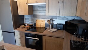 A modern kitchen with wooden cabinets, a black countertop, a toaster, a microwave, and a built-in oven. - APARTMENT FACING FONCILLON BEACH (Royan)