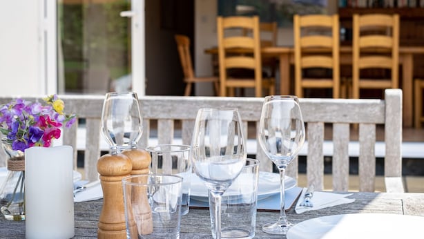 A dining table set with wine glasses, a salt and pepper shaker, and a vase with flowers. - Flaad House (Wadebridge)