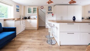 A modern kitchen with white cabinets, a wooden countertop, and two copper pendant lights. - Flaad House (Wadebridge)