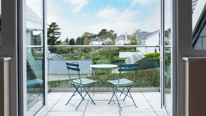 A balcony with a glass door, two blue chairs, and a small table. - Flaad House (Wadebridge)