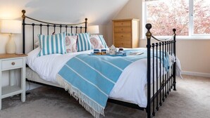 A bedroom with a bed, nightstands, a dresser, a window with a view of trees, and a ceiling light. - Flaad House (Wadebridge)
