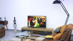 Un salon moderne avec un téléviseur à écran plat, un canapé en cuir, une table basse en verre et un lampadaire.